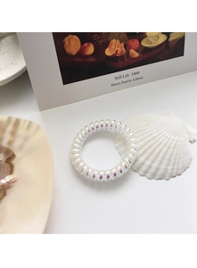 Makroaufnahme eines irisierenden Spiralhaargummis auf einer Muschel und Kunstkarte
