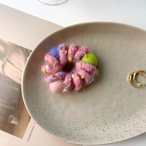 Detailed view of a pink plush spiral hair tie with a green pompom and colorful fiber spots