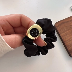 Detail of black satin scrunchie with a gold metal plate featuring a smiley face