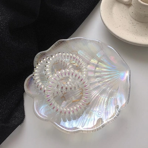 Drei perlmuttschimmernde Telefonkabel-Haargummis in einer muschelförmigen Glasschale