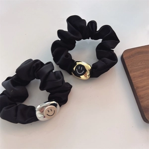 Two black satin hair scrunchies with gold and silver smiley face charms on a wooden tray