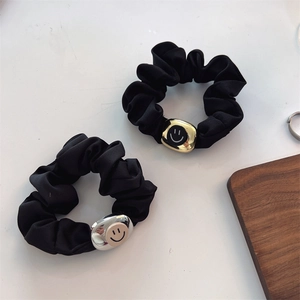 Close-up of black satin scrunchies with metallic gold and silver smiley face charms