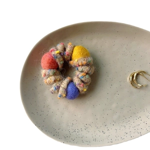 Colorful plush spiral hair tie with wool balls on a ceramic plate, 45-degree view
