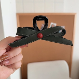 Detail of dark green leather bow hair claw clip with a red pearl and visible stitching