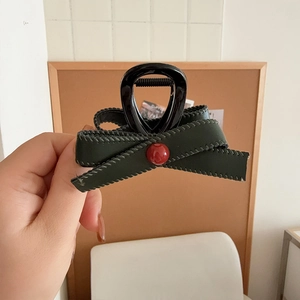 Detailed view of handmade dark green leather bow hair claw with a red pearl accent