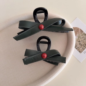 Close-up of dark green faux leather bow hair clips with red bead detail on a tray