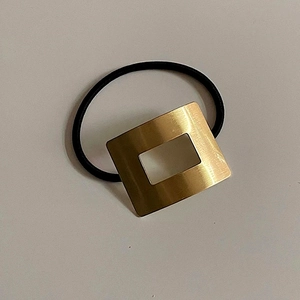 Dettaglio del rettangolo in metallo spazzolato dorato su elastico per capelli nero