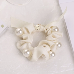Detail eines cremefarbenen Satin-Scrunchies mit großen weißen Perlen und Goldmünzen-Anhänger