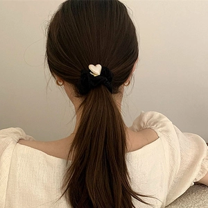 Close-up of elegant black scrunchie with cream heart charm worn on model hair