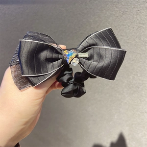 Detail of a black satin bow hair tie with a sparkling heart crystal and handmade charm