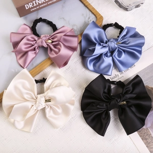 Detail of four satin bow hair ties in dusty purple, blue, beige, and black with metal buckles