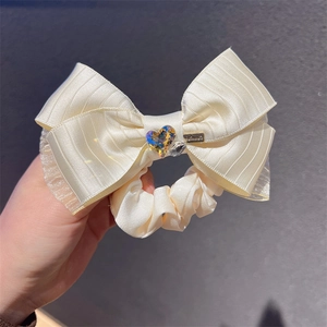 Close-up of a cream bow hair tie with heart-shaped rhinestone and Handmade tag
