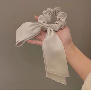 Detail view of cream satin bow scrunchie with dangling pearls and metal logo charm