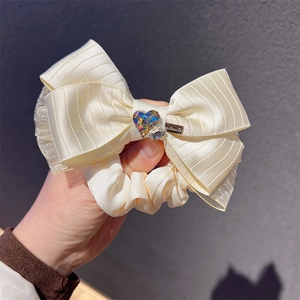 Detail of cream silk bow hair tie featuring a sparkling crystal heart and handmade charm