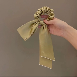 Detailed shot of champagne satin scrunchie with long ribbon and pearl accents