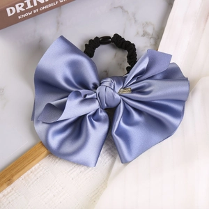 Detail of blue satin bow hair tie with metal plaque and elegant silk texture close-up