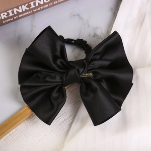 Detail of black satin bow hair tie with golden handmade metal buckle on marble surface