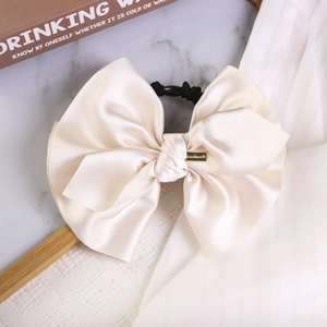 Detail of cream satin bow scrunchie with glossy texture and gold metal logo plaque