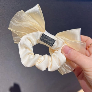 Elegant cream bow scrunchie with layered pleated texture and handmade woven label