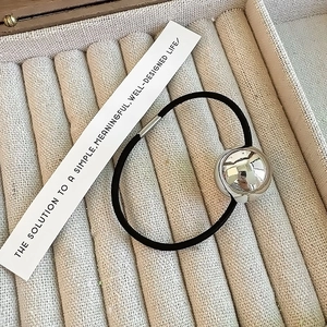 Minimalist black hair tie with large polished silver bead in a beige jewelry box tray
