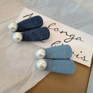 Détail de pinces à cheveux en jean avec grandes perles blanches sur textures bleues