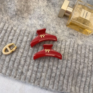 Détail de deux pinces à cheveux rouge foncé avec nœud doré sur un pull en maille gris