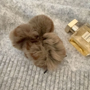 Plush brown hair claw clip detail on gray knit sweater background with perfume