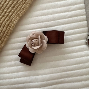 Detail of beige fabric camellia flower and dark brown satin bow hair clip on white padding