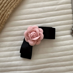 Pink camellia flower hair clip with black ribbon bow on white quilted background