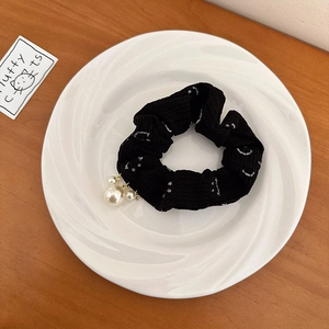 Détail de l'élastique en maille noire avec imprimé smiley blanc et pendentif perle sur assiette