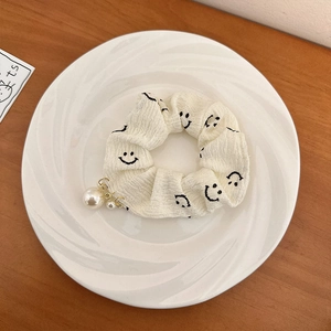 Gros plan d'un chouchou blanc avec motifs smiley et pendentifs en perles fines