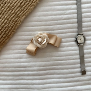 Detailed macro shot of champagne gold satin bow hair clip with camellia flower ornament