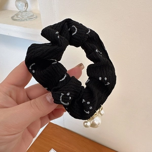 Détail d'un chouchou en tissu noir avec imprimé smiley et breloques en perles