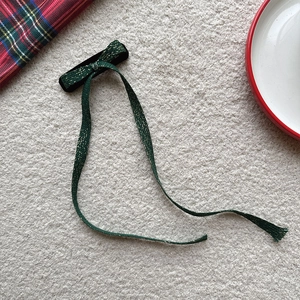 Détail d'une pince à cheveux en velours vert foncé avec rubans de soie dorés