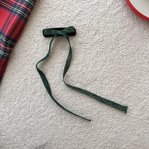 Détail d'un nœud papillon vert foncé avec coutures dorées sur fond de tissu blanc doux