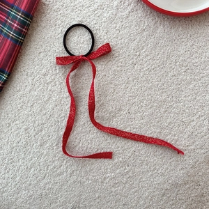 Détail d'un élastique à cheveux nœud rouge avec tissage doré sur fond beige doux