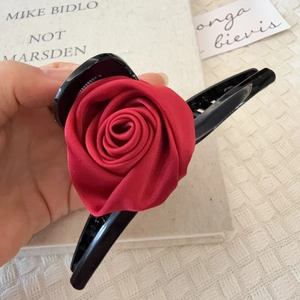 Détail d'une grande pince à cheveux noire ornée d'une rose réaliste en tissu rouge