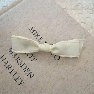 Elegant cream white ribbon bow hair clip on a minimalist textured art book background