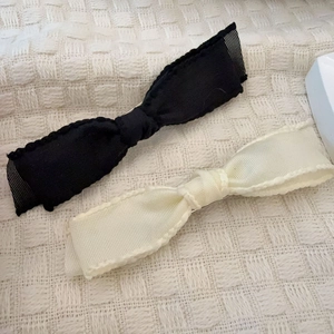 Detail view of black and beige woven bow hair clips with delicate wavy stitched edges