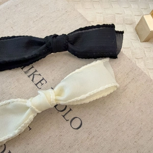 Close-up of black and beige bow hair clips with scalloped edges and textured ribbon detail