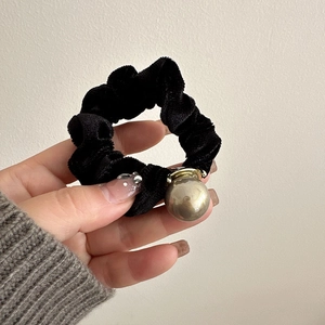 Detailed close-up of a black velvet scrunchie featuring a large glossy golden pearl detail
