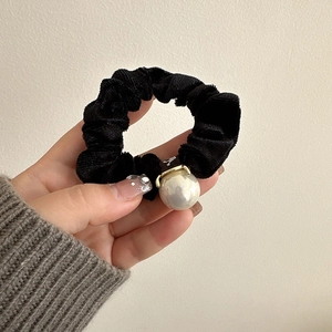 Close-up of a black velvet scrunchie featuring a large elegant white pearl pendant