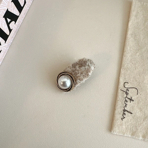 Detail of a beige faux fur hair clip featuring a large pearl with a golden twist border