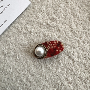 Detailed close-up of tweed hair clip with large faux pearl and golden metal button