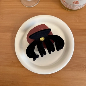 Detail of classic black velvet hair claw clip with golden metal logo on a ceramic plate