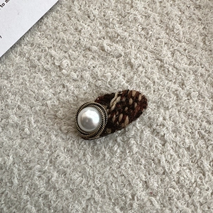 Detail of tweed hair clip featuring an elegant faux pearl button and woven fabric