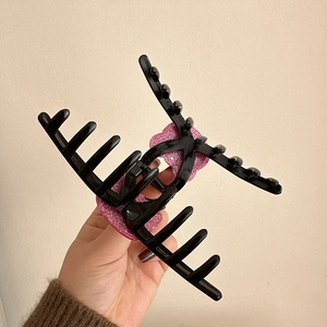 Dettaglio di una grande pinza nera per capelli con cuore glitter rosa e denti incrociati