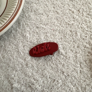 Detailed macro view of the red flocked Rich letter hair clip on a soft textured background