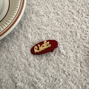 Elegant red flocked hair clip with gold Rich letter ornament on soft white background