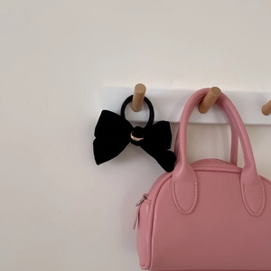 Elegant black velvet bow scrunchie with a gold ring accent hanging on a white wooden hook
